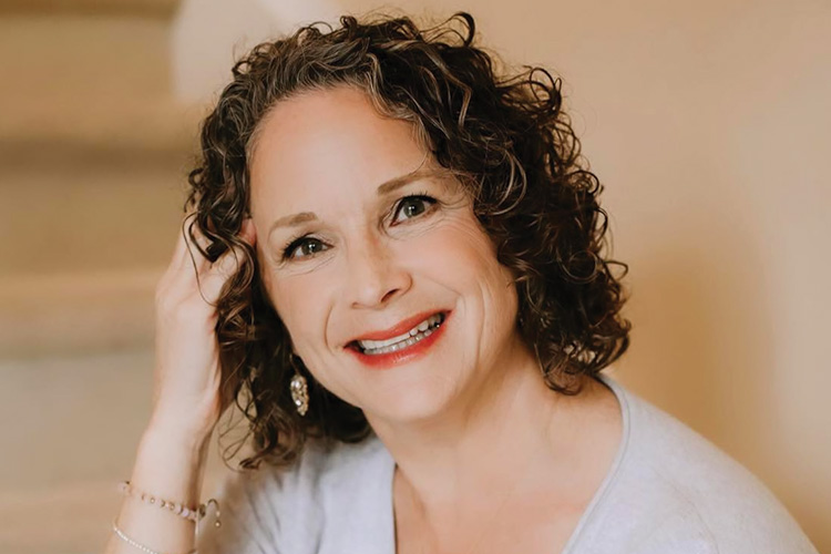 Glynnis Schwan smiling warmly, seated on steps with hand near her curls