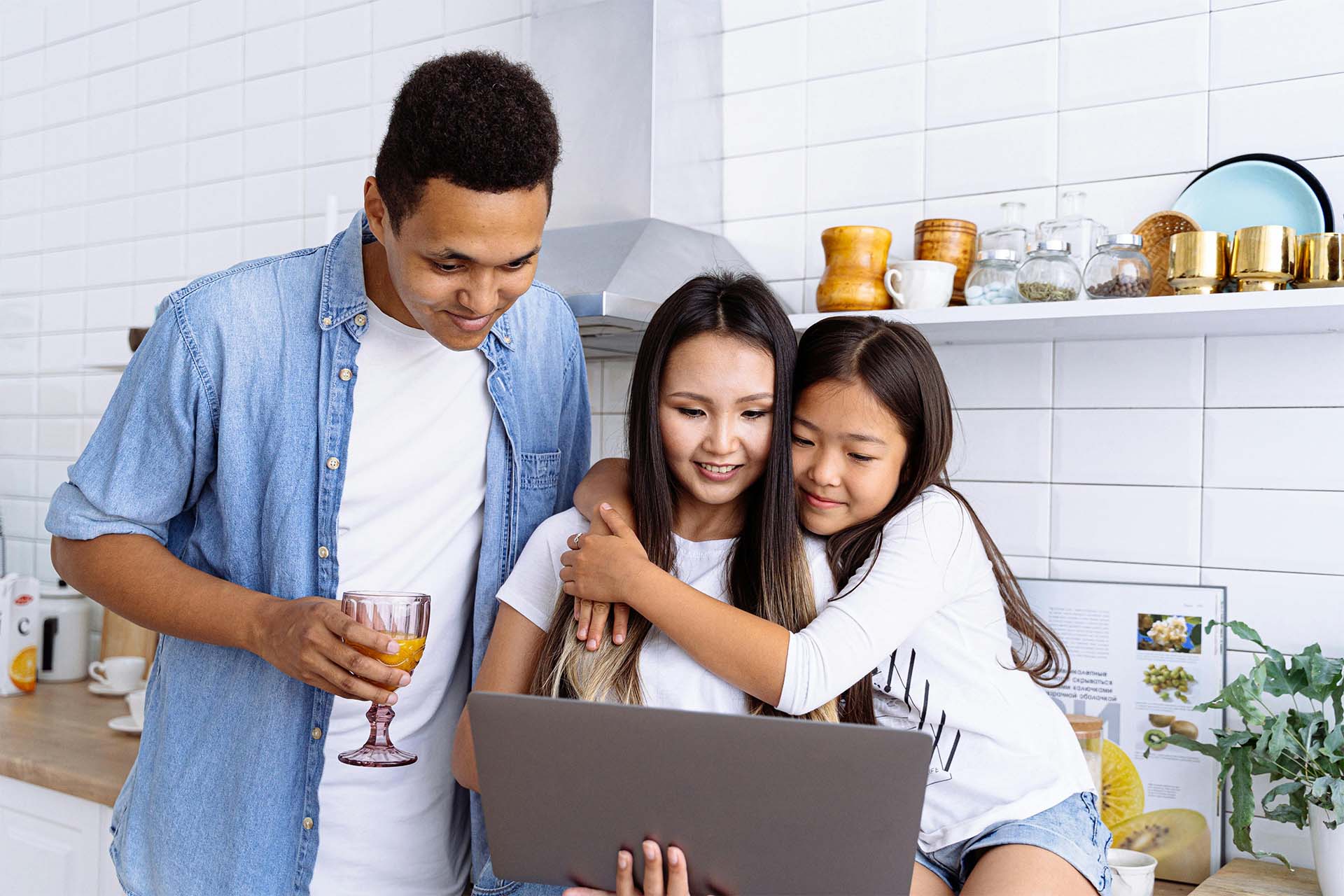 A family reading an email newsletter together on a laptop in the kitchen.