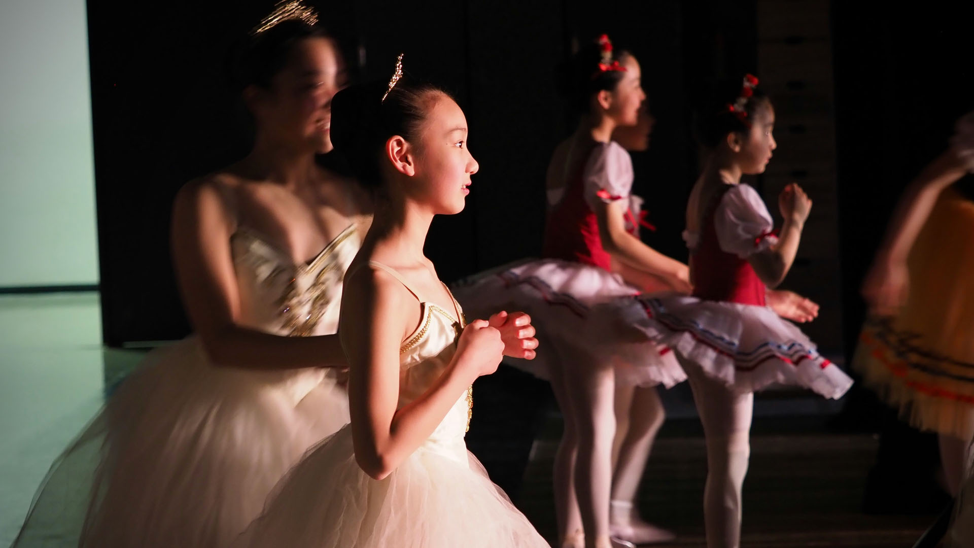 Teen ballet dancers in costume preparing backstage during recital performance.