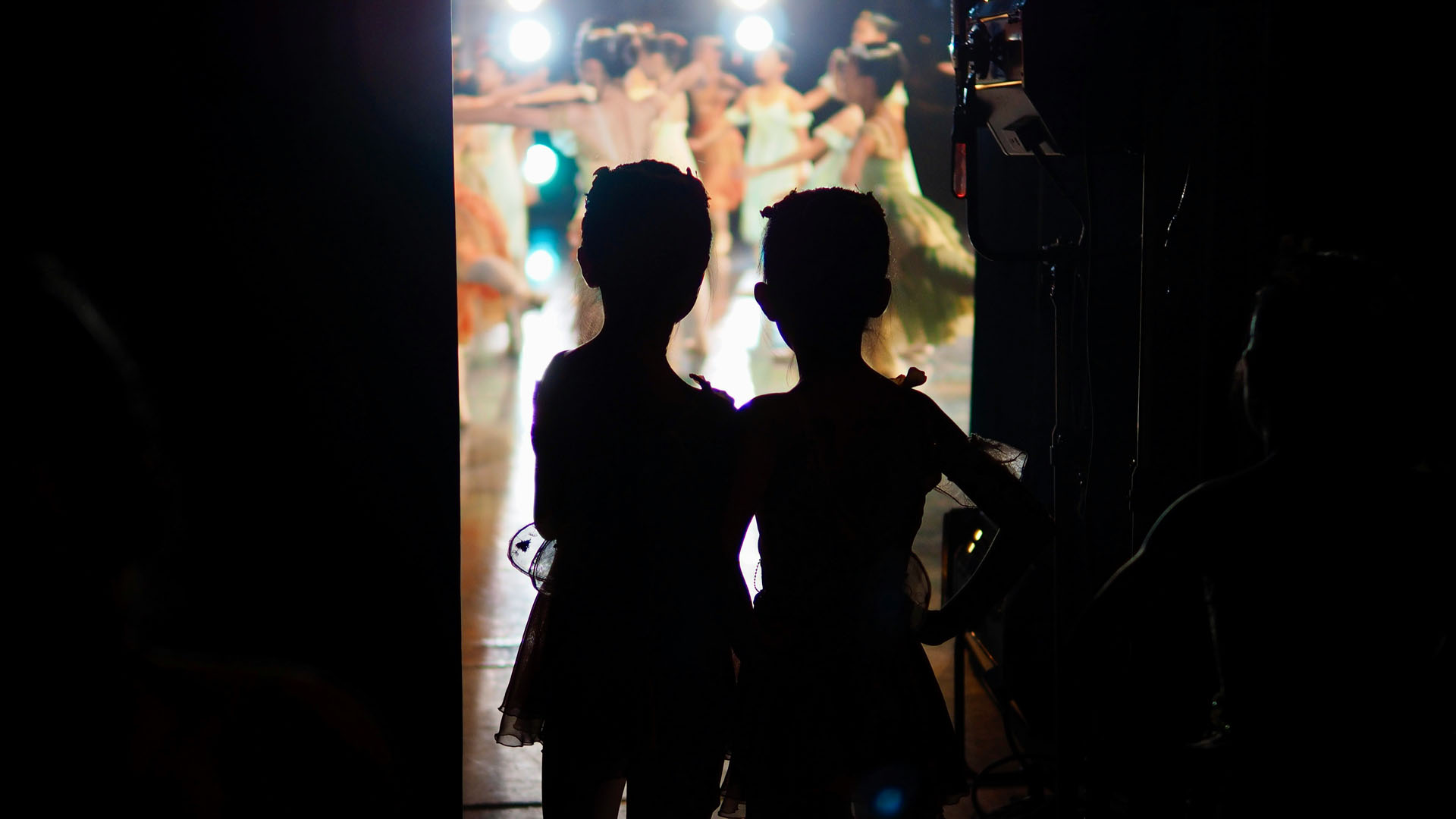 Silhouette of young dancers backstage watching a recital finale.