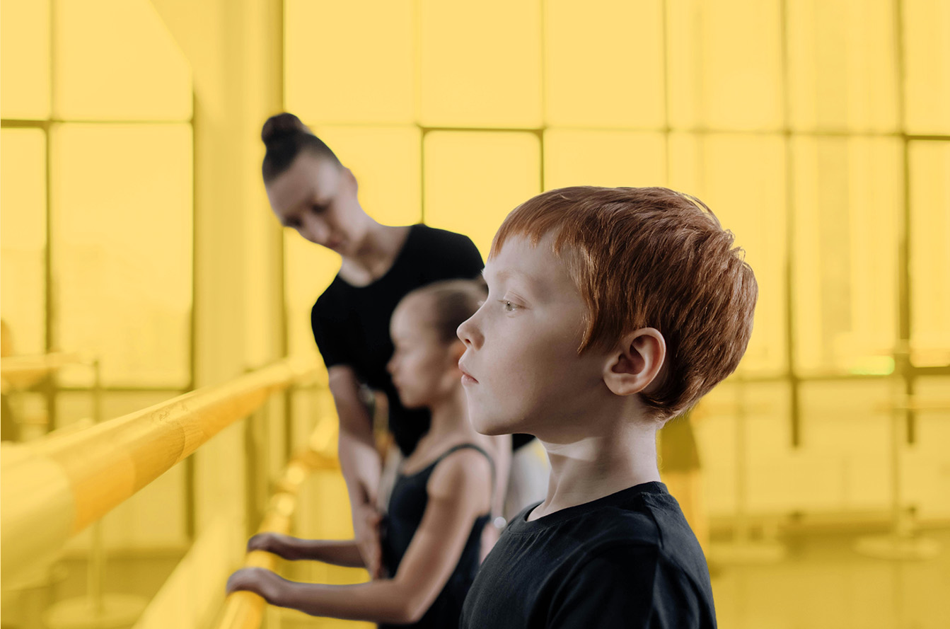 Young dancers at the barre with instructor guiding them, showcasing studio culture and mentorship.