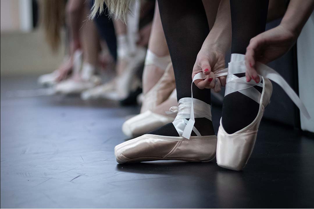 Five young ballet dancers sitting together against a studio wall.