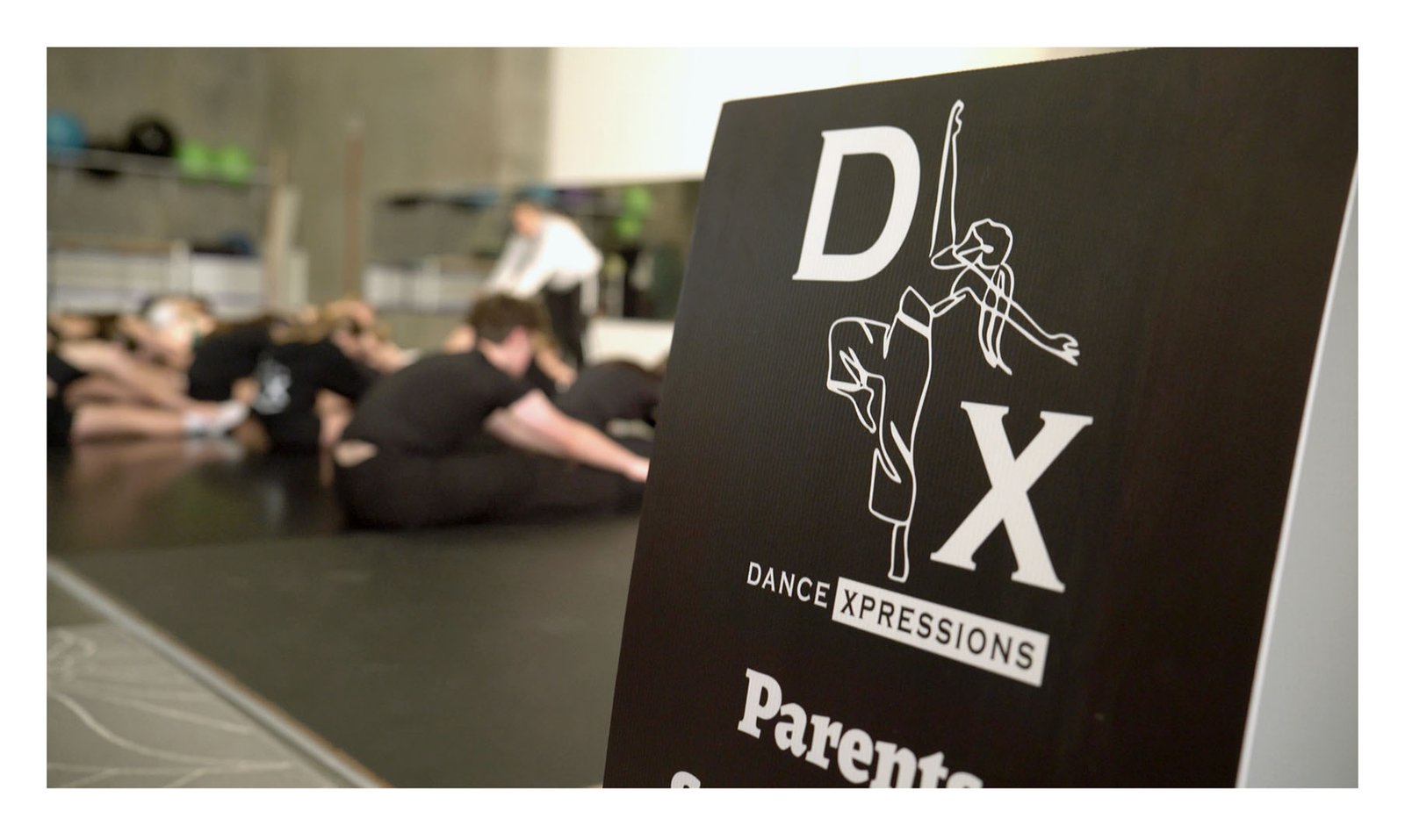 Dance Xpressions sign in the foreground while dancers rehearse in the studio